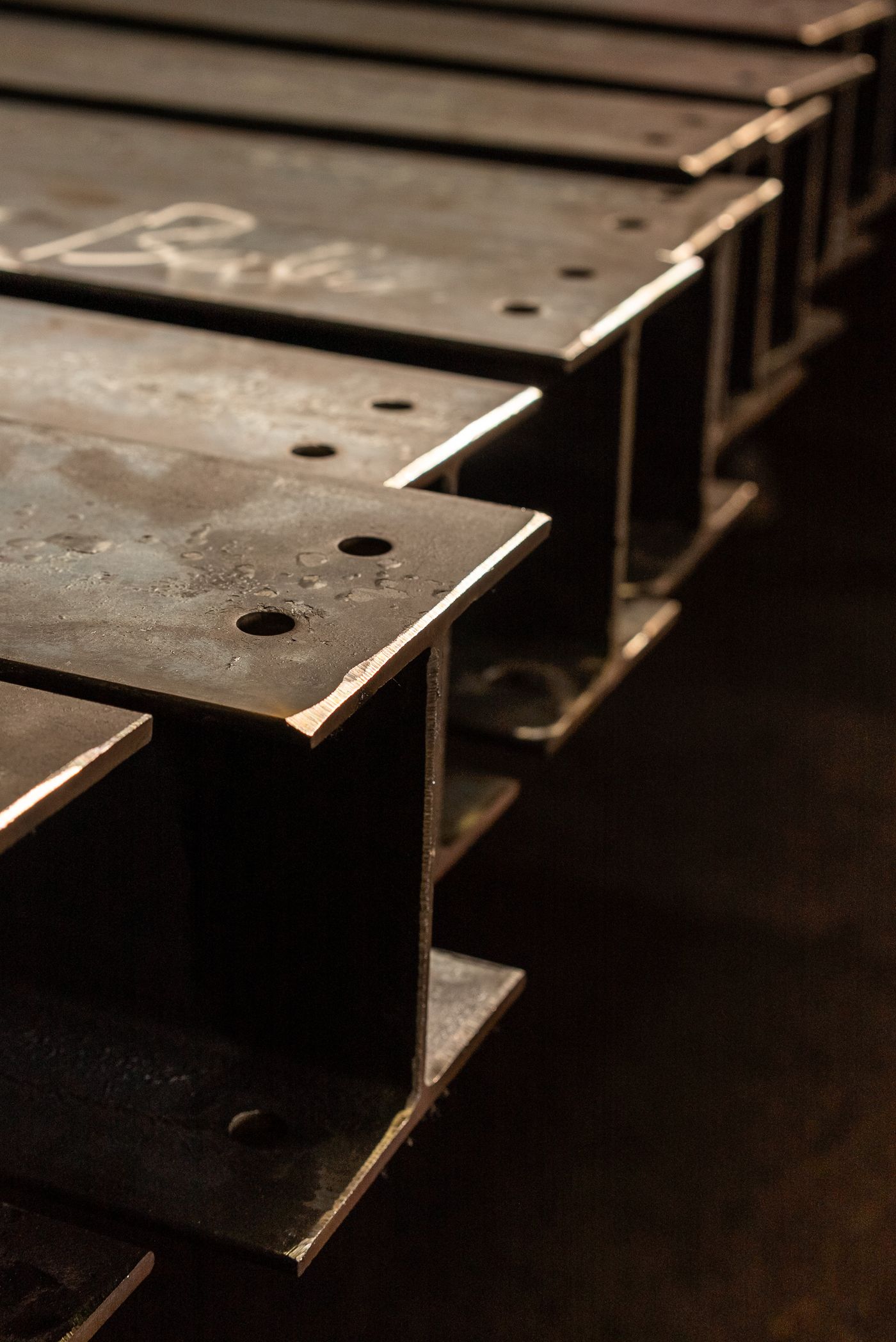 Fabricated steel I-beams with drilled connections, stacked in the shop