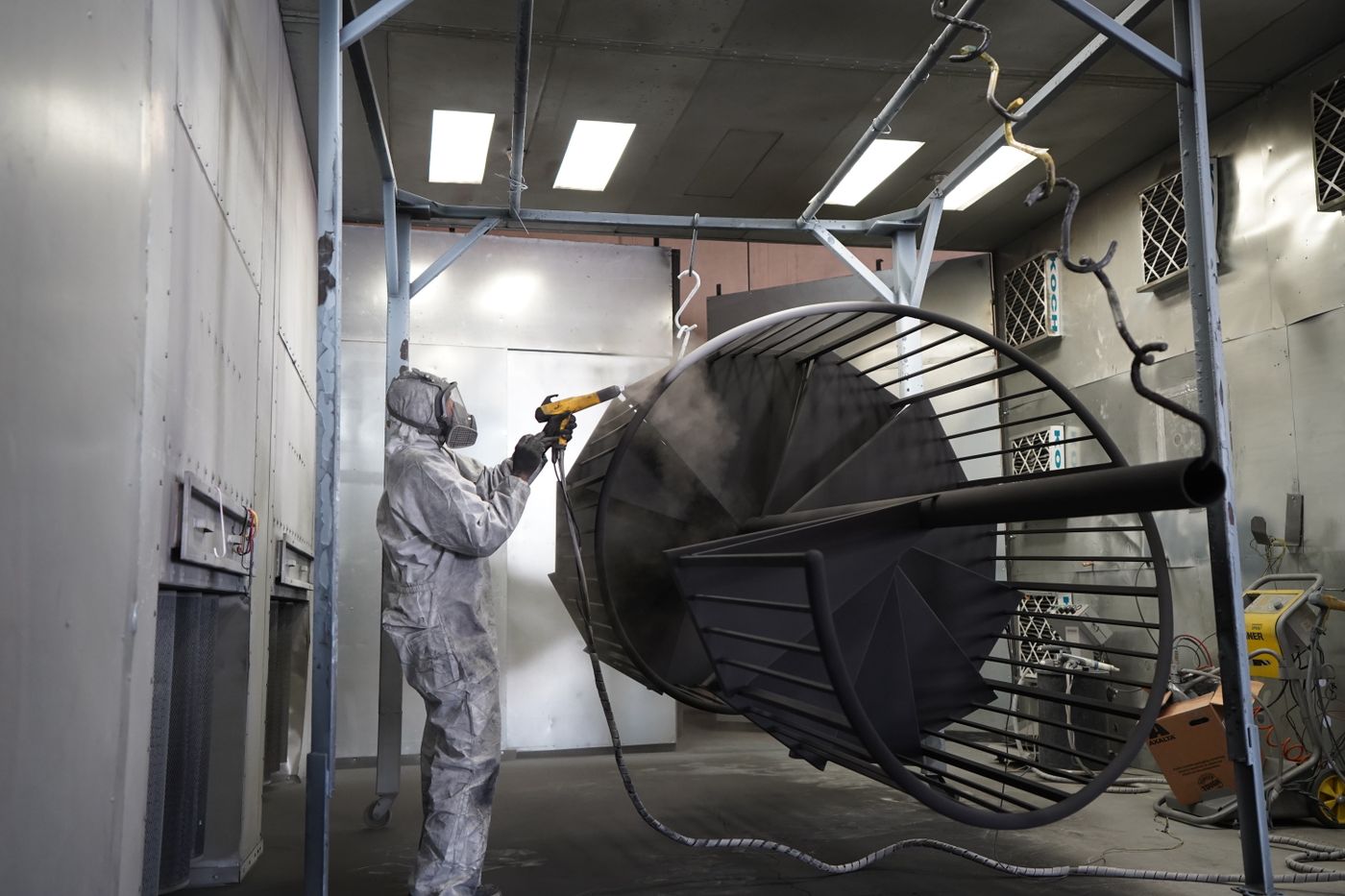 Technician powder coating a fabricated steel structure in the booth